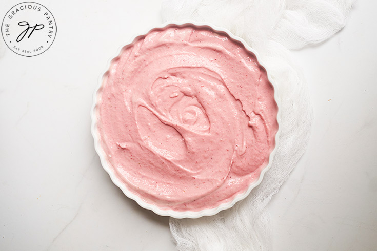 Healthy Strawberry Ice Cream spread out over a white, tart dish for freezing.