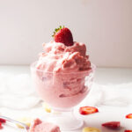 A glass parfait dish holds a serving of Healthy Strawberry Ice Cream, topped with a fresh strawberry.