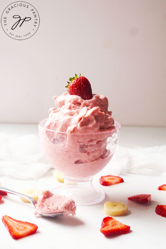 A glass parfait dish holds a serving of Healthy Strawberry Ice Cream, topped with a fresh strawberry.