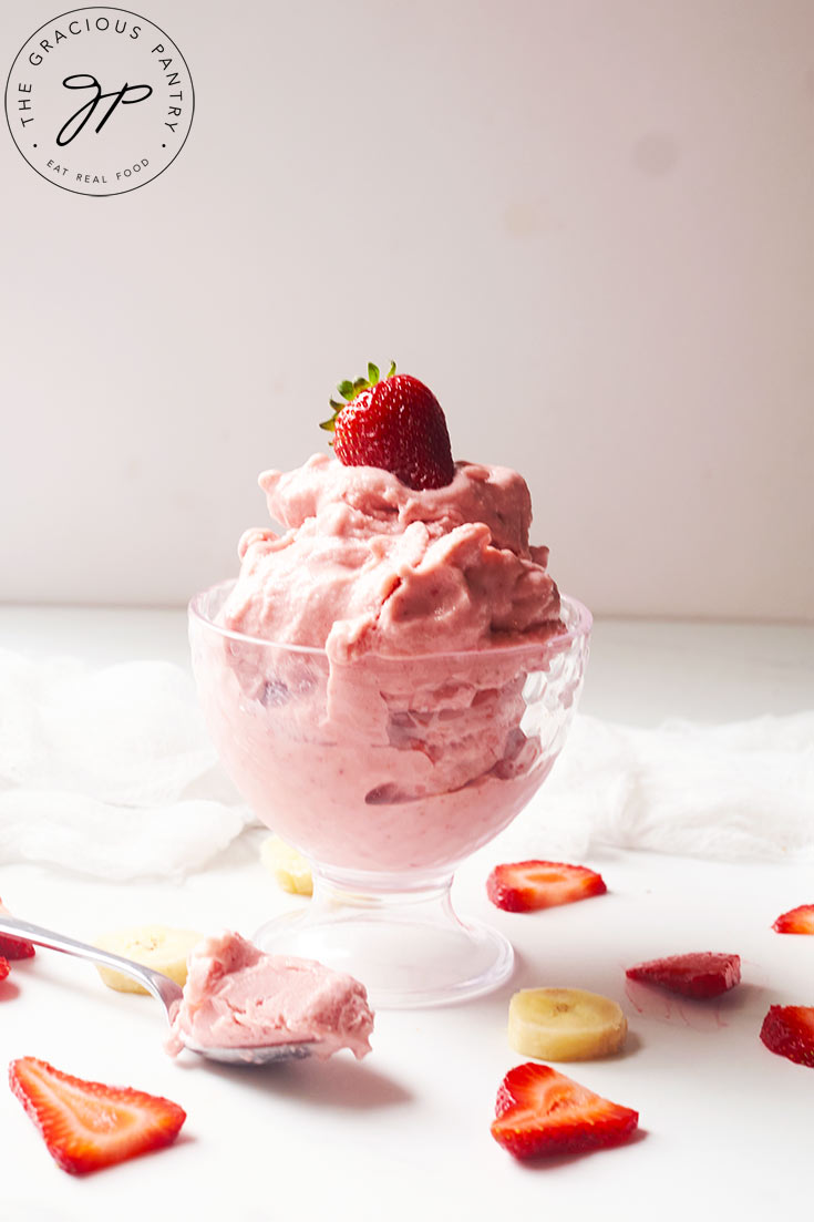 A glass parfait dish holds a serving of Healthy Strawberry Ice Cream, topped with a fresh strawberry.