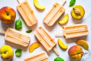 The finished Homemade Peach on a white table with fresh peach slices laying around the popsicles.