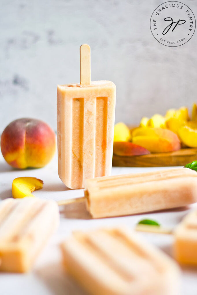 Homemade Peach Popsicles lay on a table with one popsicle standing on end.
