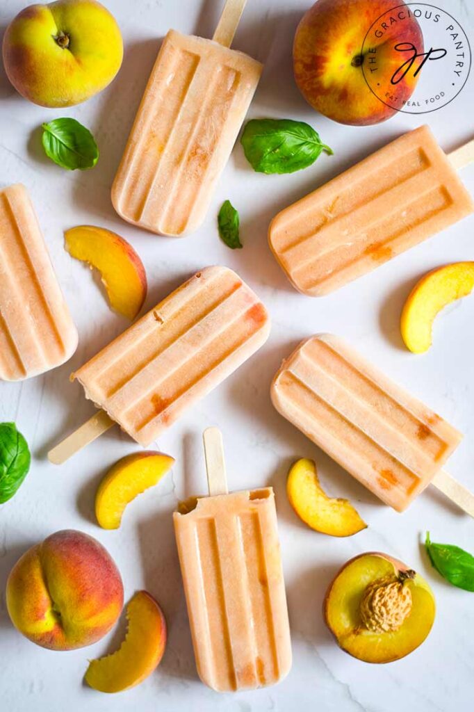 Homemade Peach Popsicles lay arranged on a white surface with fresh peaches.