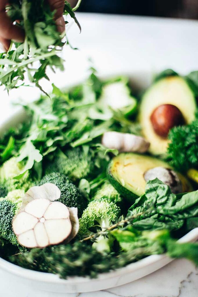 A white dish filled with fresh greens, raw broccoli and a cut avocado.