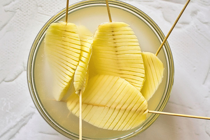 Soaking accordion potatoes to remove excess starch in a glass bowl.