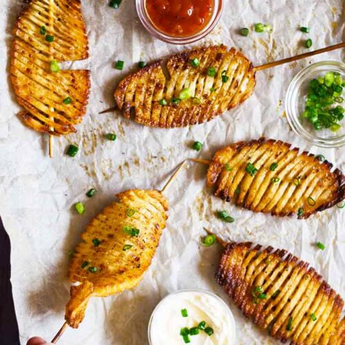 A female hand reaches for an accordion potato skewer that lays on a parchment-linked cookie sheet.