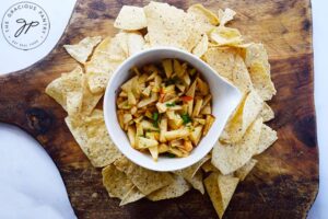 Apple salsa in a white serving bowl surrounded by corn chips on a cutting board.