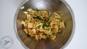 Chopped apples and minced pepper placed in a metal mixing bowl.