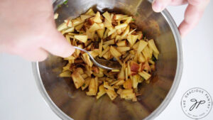 Stirring apple salsa ingredients together in a metal mixing bowl.