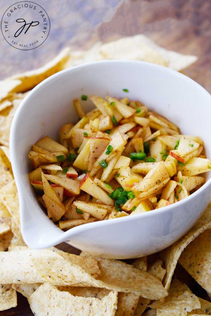 A white bowl holds apple salsa. Corn chips surround the bowl.