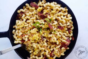 A cast iron skillet hold breakfast pasta on a white background.