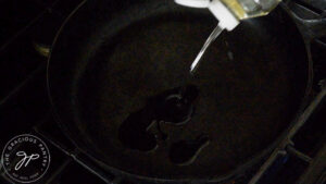 Oil being poured into a cast iron skillet.