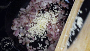 Minced garlic being added to sautéd onions in a cast iron skillet.