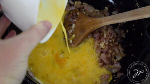 Whisked eggs being poured into a cast iron skillet.