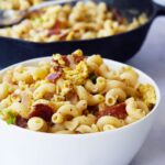 A white bowl filled with breakfast pasta sits in front of a black skillet filled with the same.