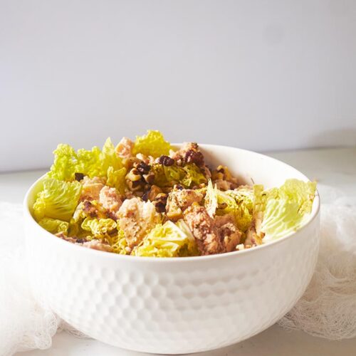 A white bowl on a white surface, filled with Chicken Endive Salad.