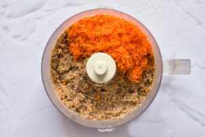 Carrots added to blended, Gluten-Free Carrot Cake crust in a food processor.