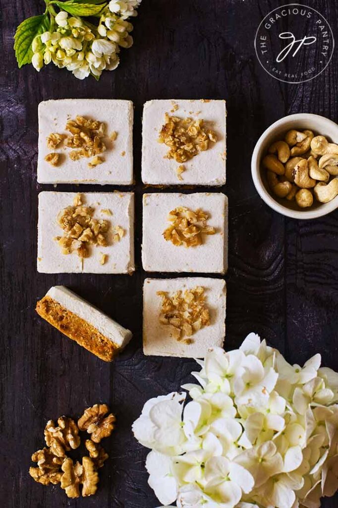 An overhead view looking down onto a dark surface which holds 6, square-cut pieces of Gluten-Free Carrot Cake .