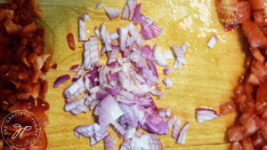 Chopped tomatoes, onions and red peppers on a wood cutting board.