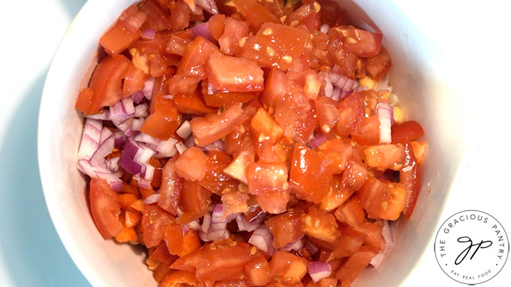 Chopped tomatoes, peppers and onions in a white mixing bowl.