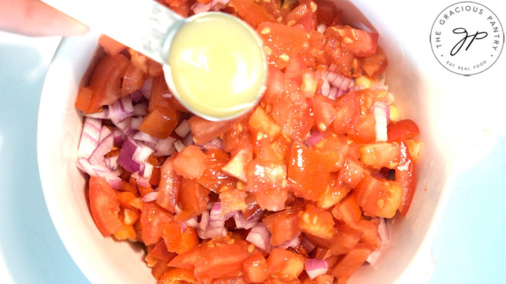 A spoonful of lemon juice being poured over chopped veggies in a white mixing bowl.