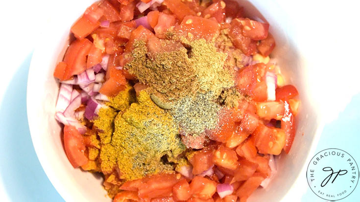 Spices added to a white mixing bowl that holds chopped veggies and chickpeas.