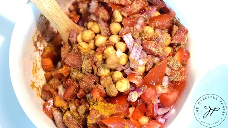 A wooden spoon mixed up this Indian Chickpea Salad in a white mixing bowl.