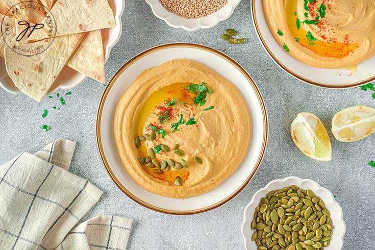 Pumpkin hummus served in white bowls and garnished with oil and pumpkin seeds.