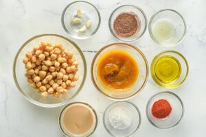 Pumpkin hummus ingredients sitting on a white surface in individual bowls.