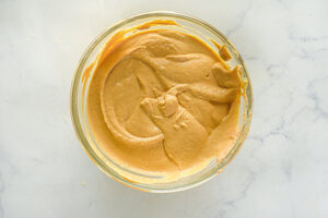 Blended pumpkin hummus in a glass mixing bowl on a white surface.