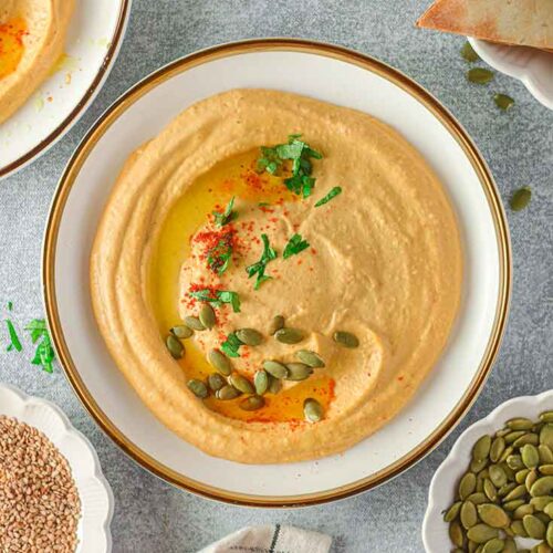 An overhead shot looking down into a white bowl with a gold rim, filled with pumpkin hummus.