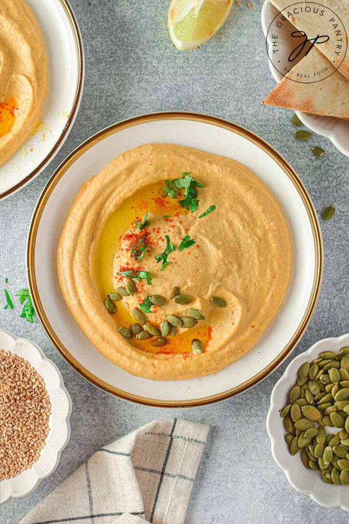 An overhead shot looking down into a white bowl with a gold rim, filled with pumpkin hummus.