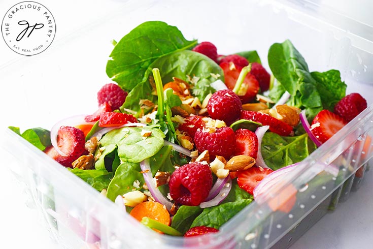 A side view of a Spinach Summer Salad in a clear, plastic container.