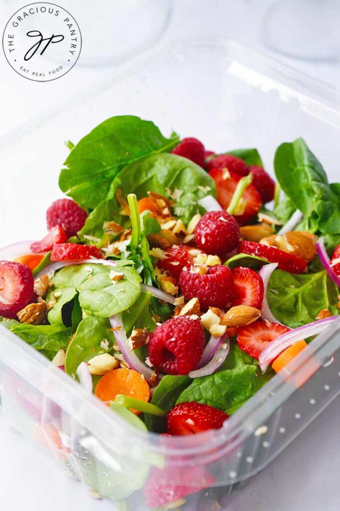 A front view of a Spinach Summer Salad in a clear, plastic container on a white background.