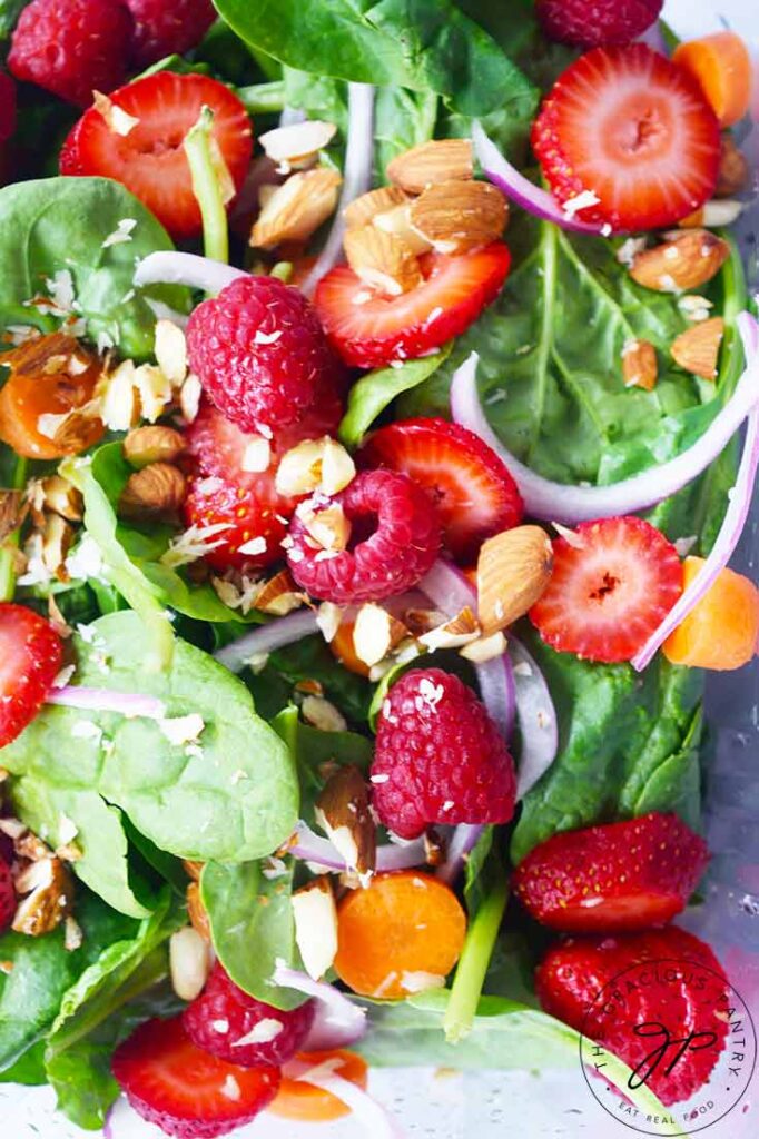 And up close view of a Spinach Summer Salad shows fresh berries, spinach, carrots, onion slices and chopped walnuts.