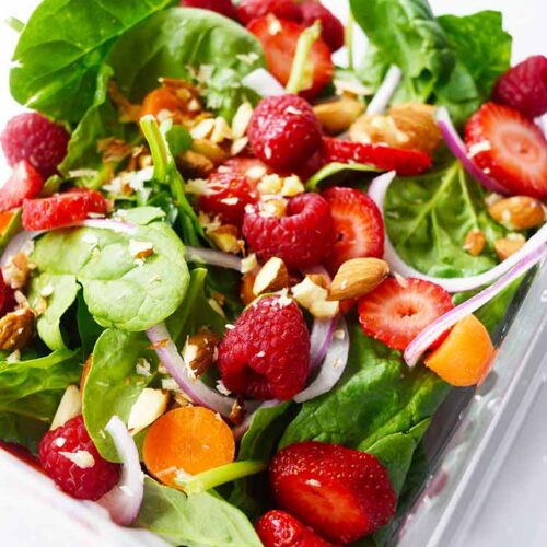 A Spinach Summer Salad sits in a clear, plastic container on a white background.