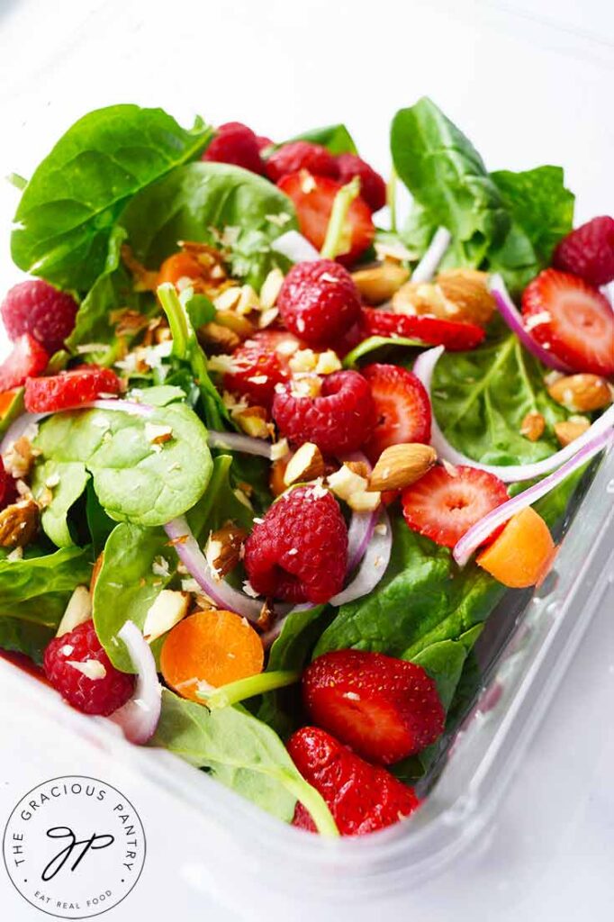 A Spinach Summer Salad sits in a clear, plastic container on a white background.