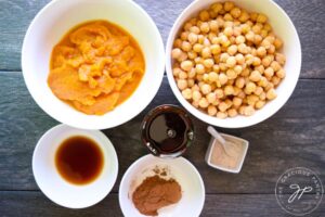 Sweet pumpkin hummus recipe ingredients in individual, white bowls on a gray surface.