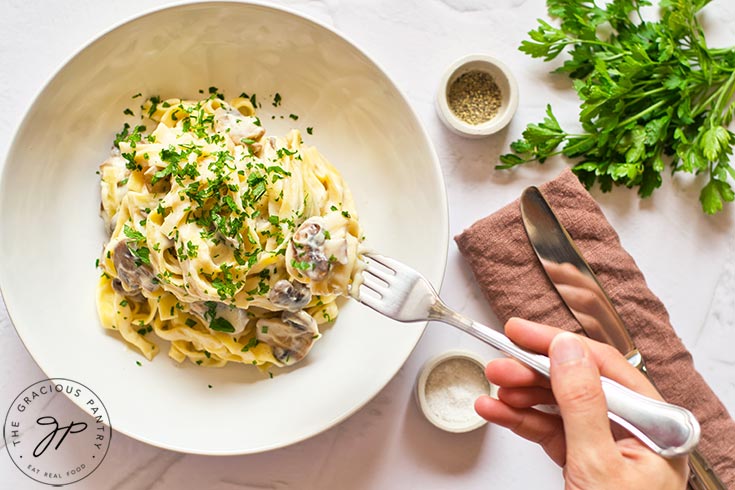 A hand holds a fork and reaches for a fork full of Vegan Fettuccine Alfredo