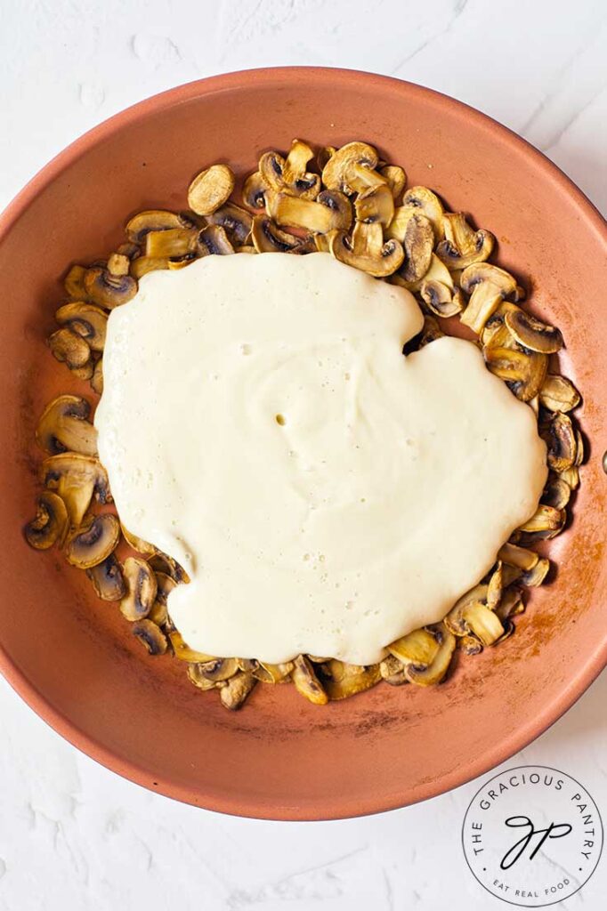 Vegan alfredo sauce poured over sautéd mushrooms in a skillet.