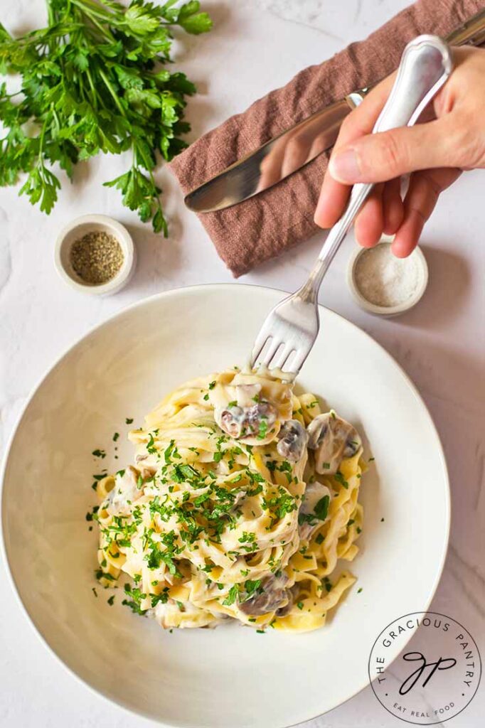 A female hands prepares to pick up a forkful of this vegan fettuccine alfredo pasta.