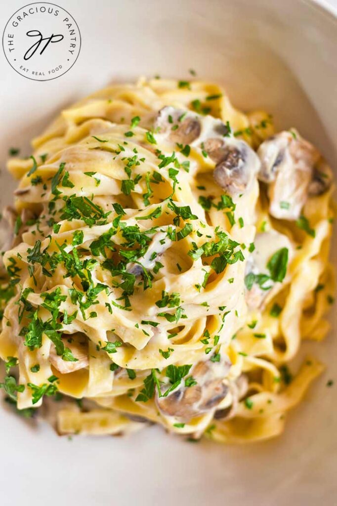 An overhead view of a white bowl holding vegan fettuccine alfredo, garnished with fresh, chopped parsley.