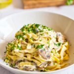 Vegan Fettuccine Alfredo served in a white bowl and garnished with fresh parsley.