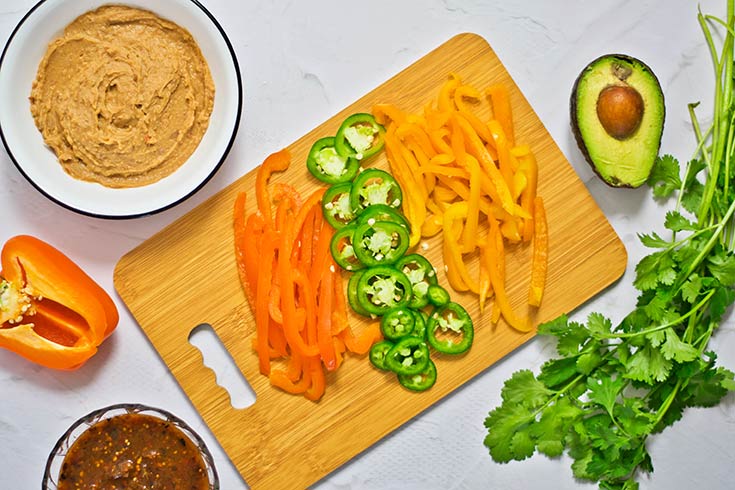 Sliced peppers for mushroom tacos laying on a wood cutting board.