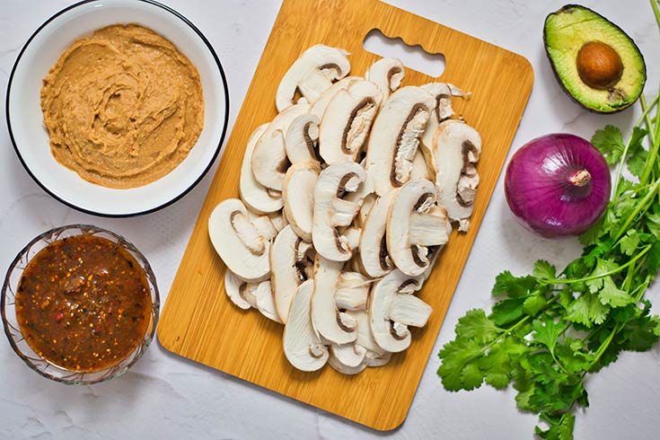 Sliced white mushrooms for mushroom tacos laying on a wood cutting board.