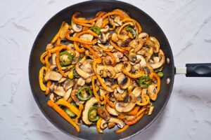 Sautéd peppers and mushrooms in a skillet.