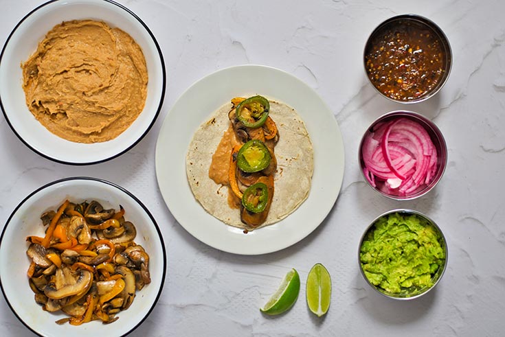 Peppers, mushrooms and refried beans layers on a corn tortilla on a white plate.