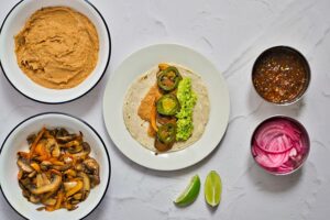 Peppers, mushrooms avocado and refried beans layers on a corn tortilla on a white plate.