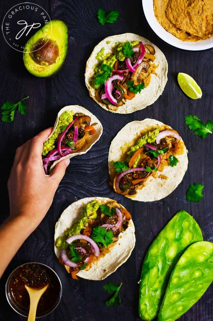 A female hand reaches for mushroom tacos sitting on a dark surface.