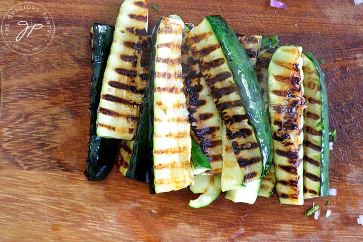 Grilled zucchini pieces laying on a wood cutting board.